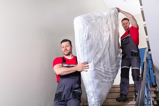 two workers hauling a box spring out of a building in Hebron